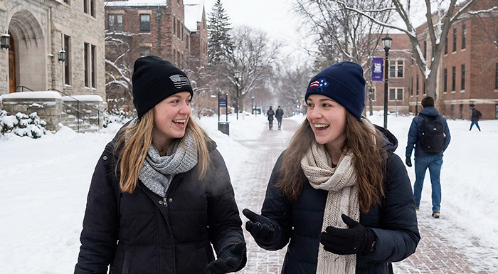 Two girls wearing patriotic beanies while waling and talking in university town