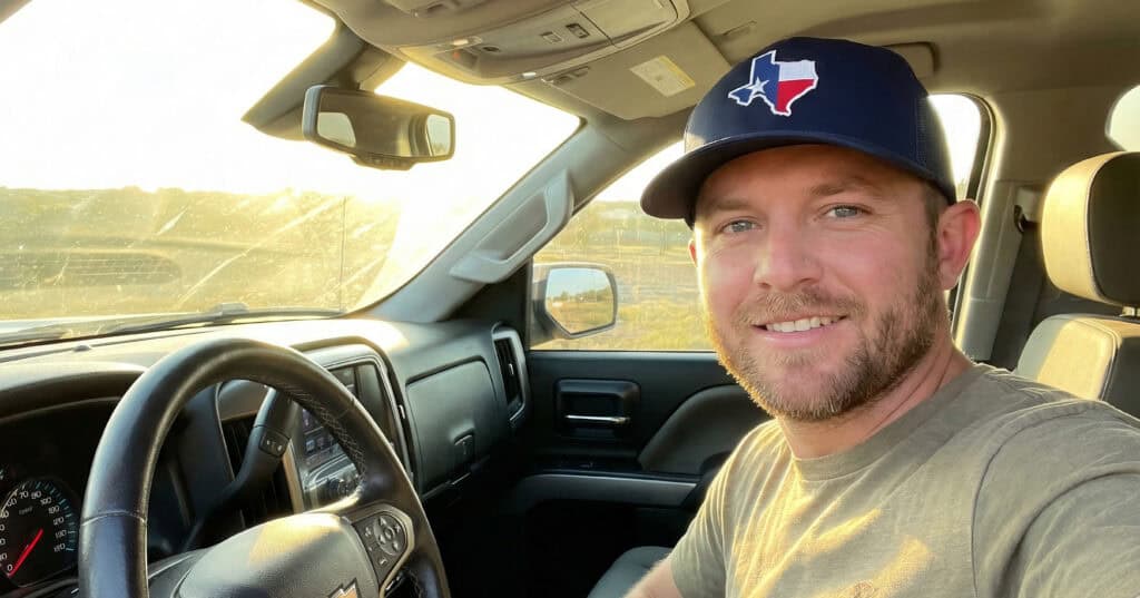 Selfie of a guy in pickup truck, wearing Texas trucker hat