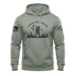Patriotic Bigfoot hoodie with American flag and forest design in sage green. Perfect for outdoor ent.