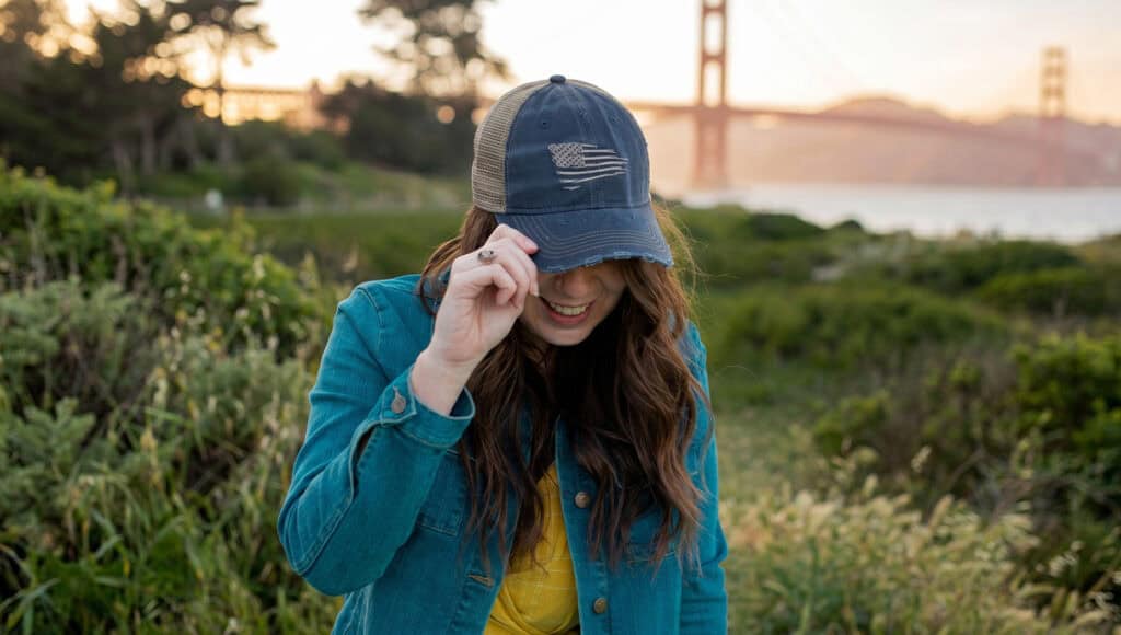 Woman wearing patriotic hat and denim jacket outdoors near Golden Gate Bridge.