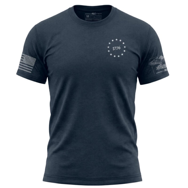 Navy blue T-shirt with "1776" and stars emblem, American flag patch on sleeve, patriotic design.