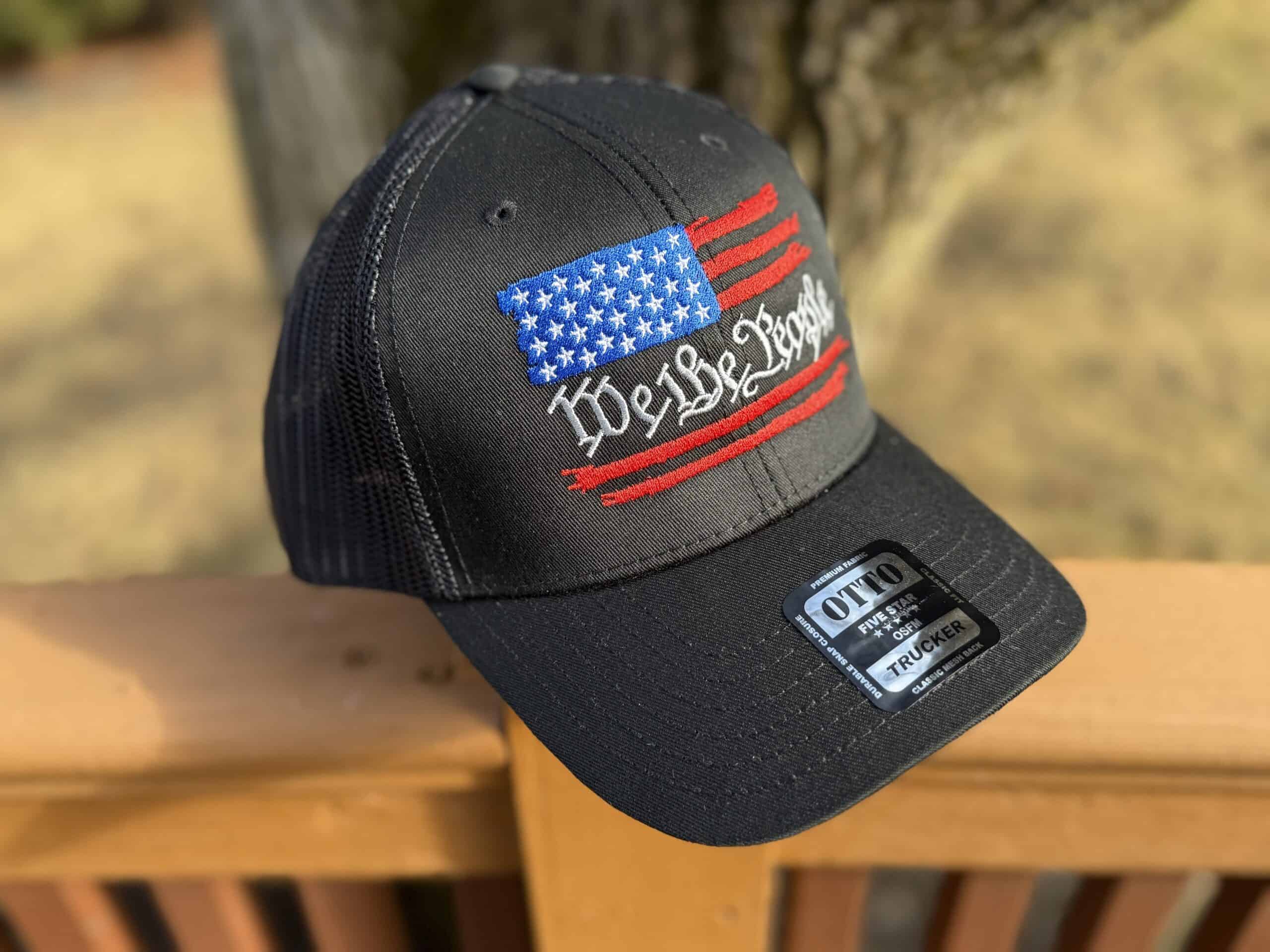 Black trucker hat with American flag and 'We the People' embroidery.