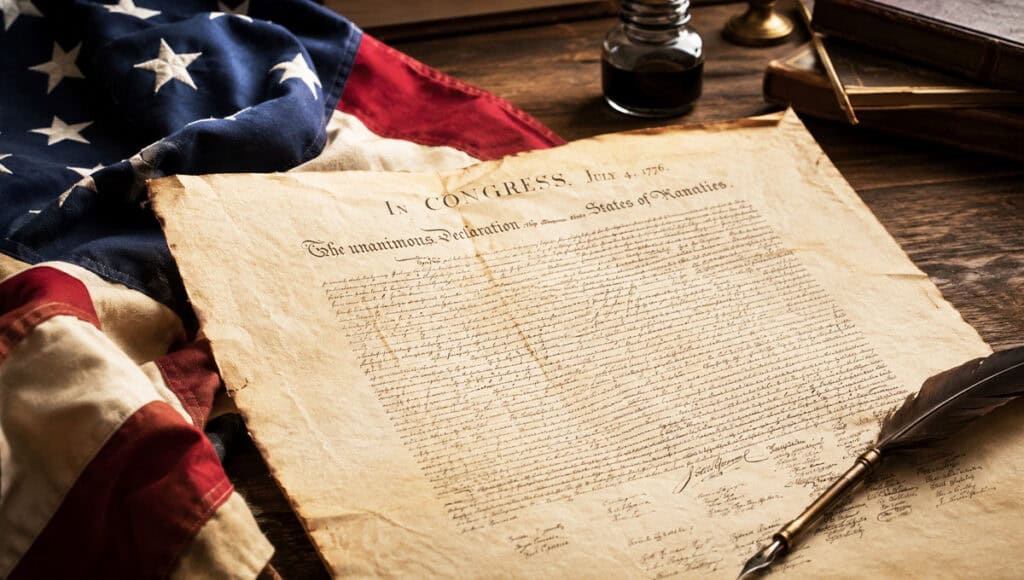Historical Declaration of Independence with American flag and quill pen.