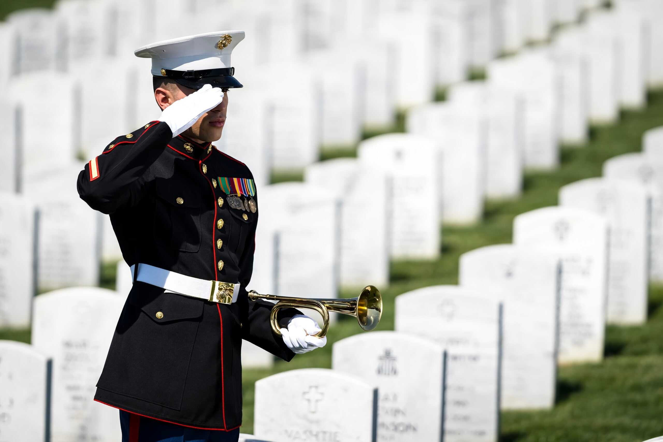 Military honor guard salutes at a cemetery with white headstones.