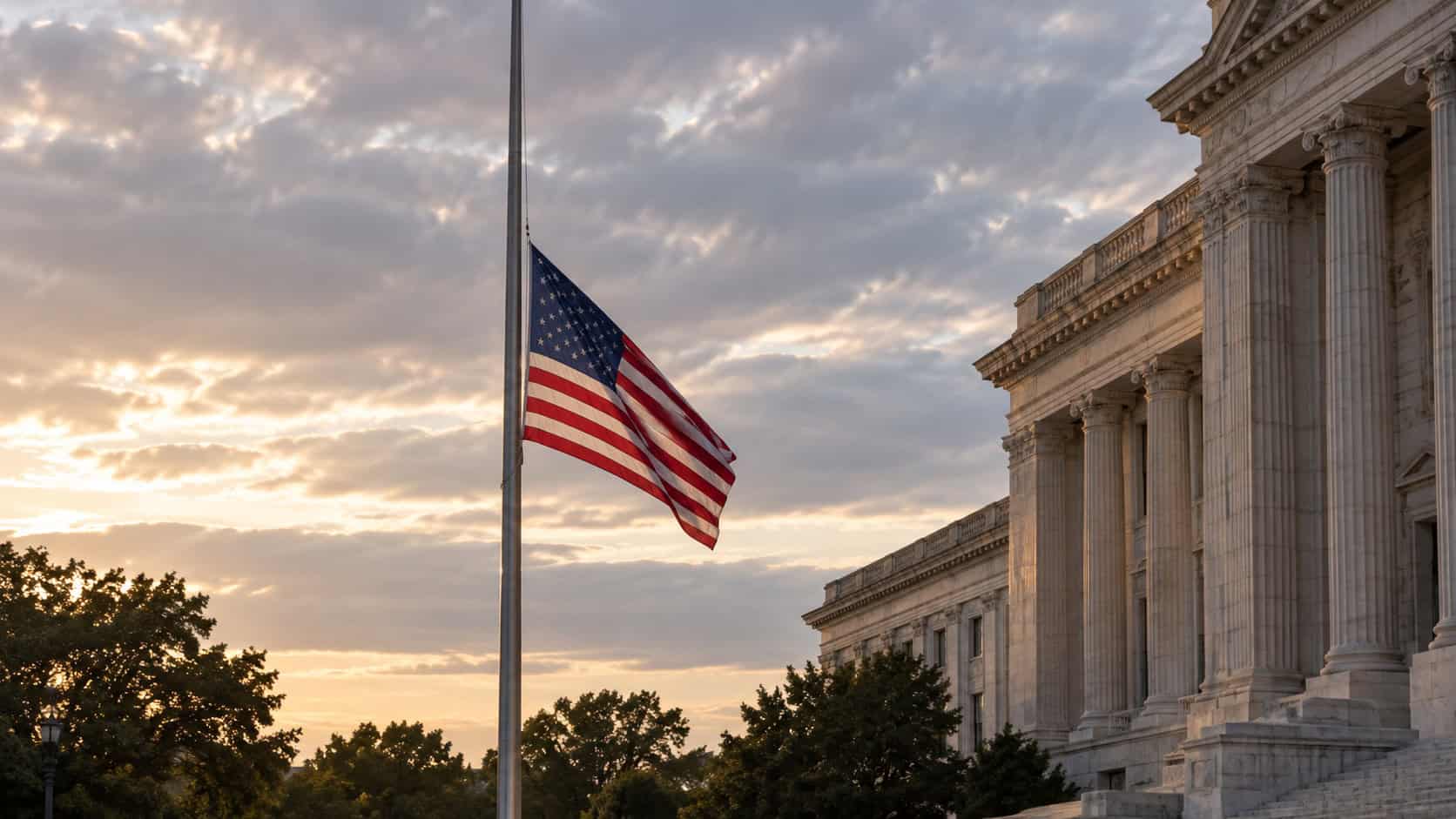 American flag flying at half-staff outside a government building under a subdued sky